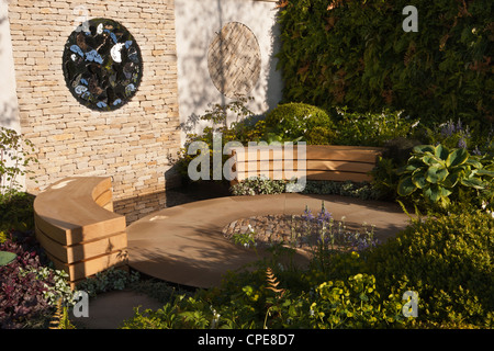 Cottage cortile giardino con parete di pietra a secco cotswold e circolare zona patio circolare e panchine in legno panca e una siepe confine UK Foto Stock