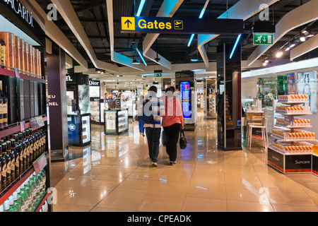 Passeggeri vai al gate di partenza attraverso negozi duty free all'Aeroporto di Manchester, Inghilterra. Foto Stock