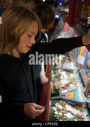 Un pre-teen boy giocando un penny per macchina a cascata in un divertimento arcade. Foto Stock