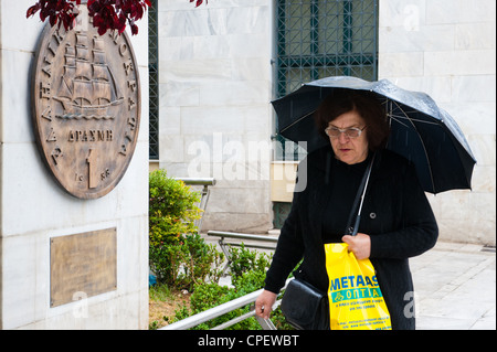 I Greci a piedi da una lapide raffigurante una vecchia dracma moneta che è stato sostituito dall'euro nel 2002 fuori Athens City Hall Foto Stock