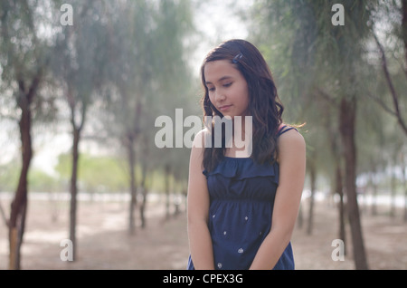 A dodici anni di razza mista ragazza (Asiatico/Caucasica) pone in un boschetto di alberi piccoli - La retroilluminazione e guardando al di fuori della fotocamera (in basso) Foto Stock