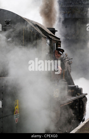 Autista del treno a vapore che guarda indietro, aspettando il permesso di partire con il suo treno ricreando una scena di viaggio comunemente vista negli anni '40, '50 e '60 Foto Stock