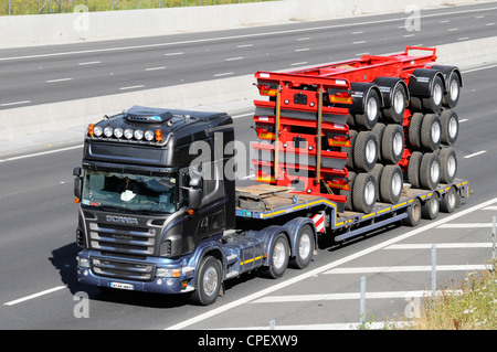 Autocarro nero il traino di rimorchio a pianale ribassato che porta una pila di camion rimorchio componenti Foto Stock