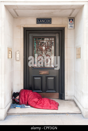 Senzatetto uomo dorme in modo irregolare a porta a Mayfair, London, England, Regno Unito Foto Stock