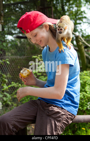 Ragazza giovane con comuni di Scimmia di scoiattolo (Saimiri sciureus) sulla sua schiena al parco Serengeti di Hodenhagen, Bassa Sassonia, Germania Foto Stock