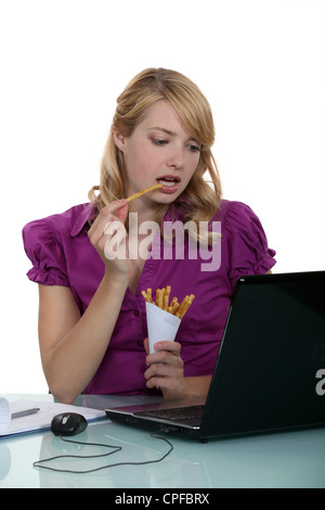 Addetto alla donna di mangiare patatine fritte alla sua scrivania Foto Stock