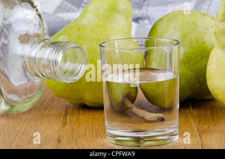 Acquavite di frutta in un bicchiere e pere fresche in background Foto Stock