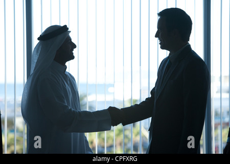 Silhouette di due imprenditori stringono le mani in una sala conferenze. Foto Stock