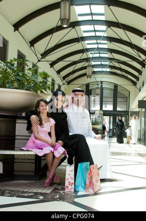 Ritratto di famiglia araba seduta al centro commerciale per lo shopping, sorridente. Foto Stock