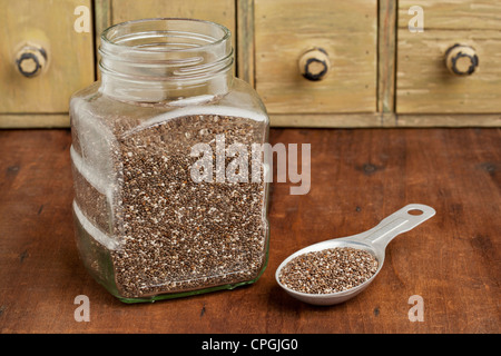 Semi di chia nel vasetto di vetro e sulla misurazione di cucchiaio di alluminio con un vintage armadio con cassetti in background Foto Stock