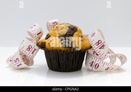 Chocolate Chip muffin con nastro di misurazione raffiguranti concetto che mangiare torte saranno pila in pollici Foto Stock