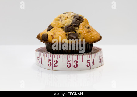 Chocolate Chip muffin con nastro di misurazione raffiguranti concetto che mangiare torte saranno pila in pollici Foto Stock