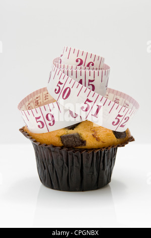 Chocolate Chip muffin con nastro di misurazione raffiguranti concetto che mangiare torte saranno pila in pollici Foto Stock