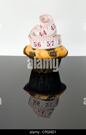 Chocolate Chip muffin con nastro di misurazione e di riflessione che raffigura il concetto che mangiare torte saranno pila in pollici Foto Stock