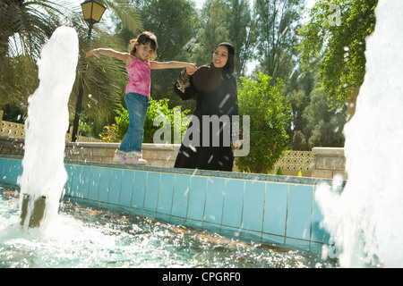 Madre e figlia in piedi da Fontana al park, sorridente Foto Stock