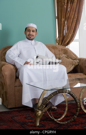 Uomo arabo seduti in un divano tenendo un giornale Foto Stock