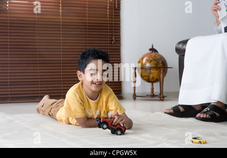 Ragazzo disteso sul pavimento, giocando giocattolo auto Foto Stock