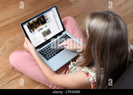 Giovane donna seduta con torna alla videocamera utilizzando il suo computer portatile su una timeline di Facebook pagina. Foto Stock
