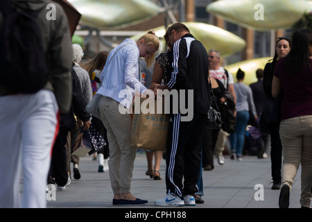 Gli amanti dello shopping in pausa sulla trafficata passerella per il Westfield Stratford Mall, a controllare gli acquisti da Primark. Foto Stock