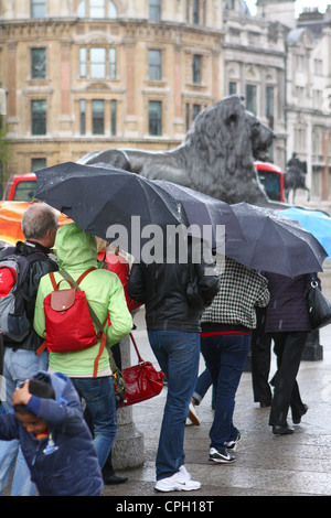 Persone che camminano in Trafalgar Square,Londra, e riparo sotto i loro ombrelloni durante una doccia di pioggia Foto Stock