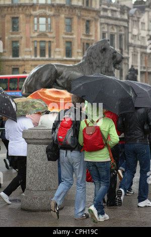 Persone che camminano in Trafalgar Square,Londra, e riparo sotto i loro ombrelloni durante una doccia di pioggia Foto Stock