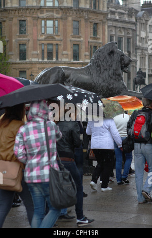 Persone che camminano in Trafalgar Square,Londra, e riparo sotto i loro ombrelloni durante una doccia di pioggia Foto Stock