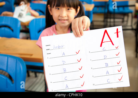 Sorridente bambina che mostra la carta di esame con un plus in classe Foto Stock