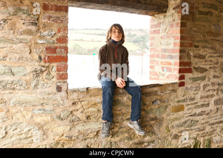 Ragazzo seduto su un muro di mattoni Foto Stock
