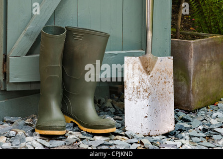 Coppia di verde stivali da pioggia e una vanga al di fuori di una Tettoia da giardino. Foto Stock