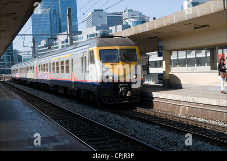 Un " commuter " treno arriva a Bruxelles Nord Station. Il treno elettrico è alimentato. Bruxelles quartiere degli affari in background Foto Stock