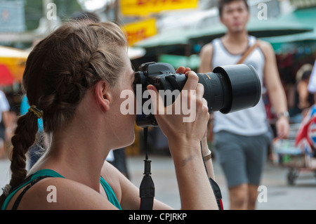 Femmina caucasica fotografo di scattare foto da parte dei visitatori del mercato Chatuchak Jatujak Bangkok in Thailandia del sud-est asiatico Foto Stock