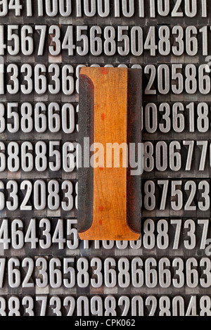 Il numero uno nella stampa tipografica vintage tipo legno sullo sfondo casuale di numeri di metallo Foto Stock