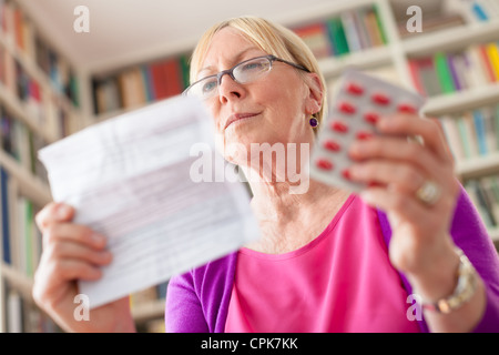 Anziana donna caucasica con la medicina e la lettura di prescrizione di farmaco. Basso angolo di visione Foto Stock