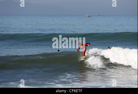 L'uomo surf in un costume da supereroe su un'onda in Java. Foto Stock