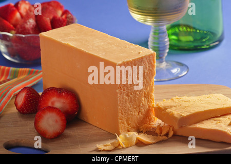 Un blocco di età compresa tra il giallo il formaggio cheddar affettare sul tagliere con fragole e sciolto in una piccola ciotola con un tovagliolo striato. Foto Stock