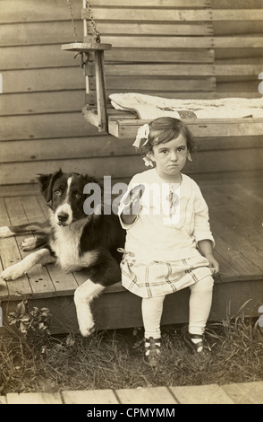 Bambina con il giocattolo rotto seduti sulla veranda con il cane Foto Stock