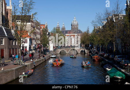 Una soleggiata Domenica porta le persone e barche per Oudezijds Voorburgwal, uno di Amsterdam i canali più frequentati. Foto Stock