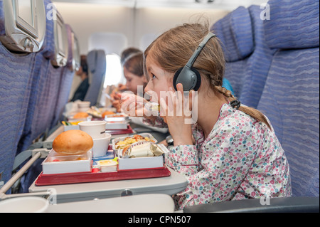 Ragazza guardando film su aereo mentre mangia pasto della compagnia aerea Foto Stock