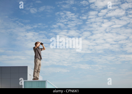 Oversized uomo in piedi su un tetto, guardando attraverso il binocolo Foto Stock