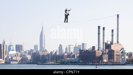 Imprenditore sovradimensionato camminando sulla fune sopra la città, portando nella valigetta farcita con pagamento in contanti Foto Stock