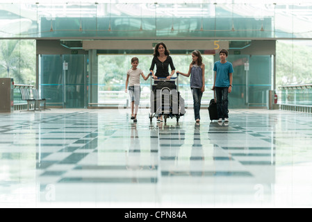 Famiglia spingendo il carrello bagagli in aeroporto lobby Foto Stock