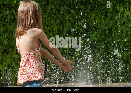 Ragazza che gioca in acqua nella fontana pubblica, vista posteriore Foto Stock