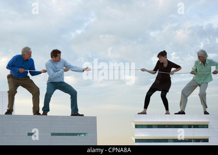 Grandi Uomini e donna in piedi sui tetti, giocando Tug-of-War Foto Stock
