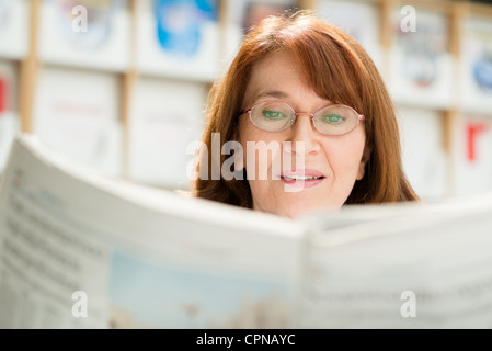 Ritratto di donna di mezza età con occhiali lettura carta in biblioteca Foto Stock