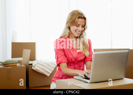 Giovane donna utilizzando il computer portatile mentre circondato da scatole di cartone Foto Stock