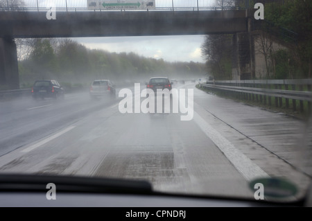 La guida su una autostrada bagnata con un overhead sign in inglese raccontando ai conducenti di guancia la distanza dalla parte anteriore auto Foto Stock