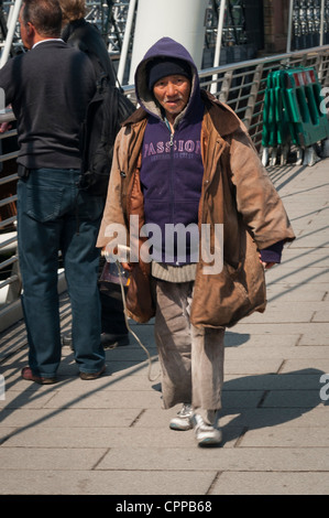 Londra , Southbank , Riverside , Embankment , Hungerford Bridge decrepito vecchio suonatore ambulante asiatico mendicante a piedi con guitar summer sun Foto Stock