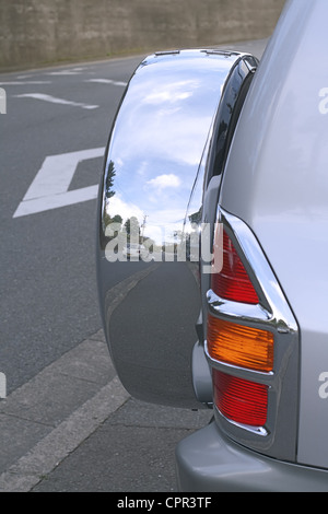 Immagine di una macchina su una strada si riflette in una ruota laterale di una jeep Foto Stock