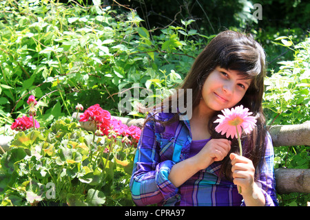 Piuttosto di otto anni ragazza seduta nel giardino tenendo un fiore rosa Foto Stock