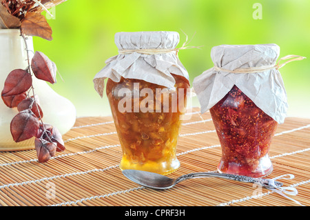 Due vasi di marmellata di frutta e un cucchiaio su sfondo naturale Foto Stock